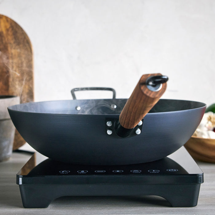 Black wok with wooden handle on an induction cooktop