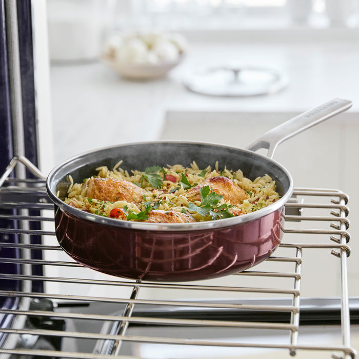 Chocolate brown enameled 2-quart sauté pan with lid on an oven rack.