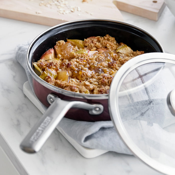 Apple crisp in a chocolate brown enameled steel 2-quart sauté pan with lid visible in the background.