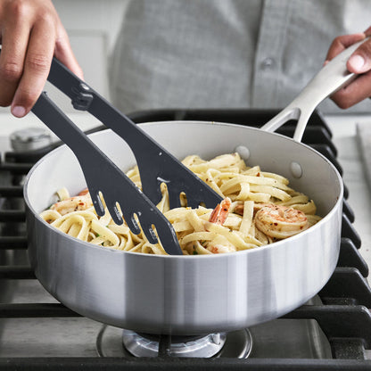 Person using silicone pasta tongs to grasp pasta in a saute pan