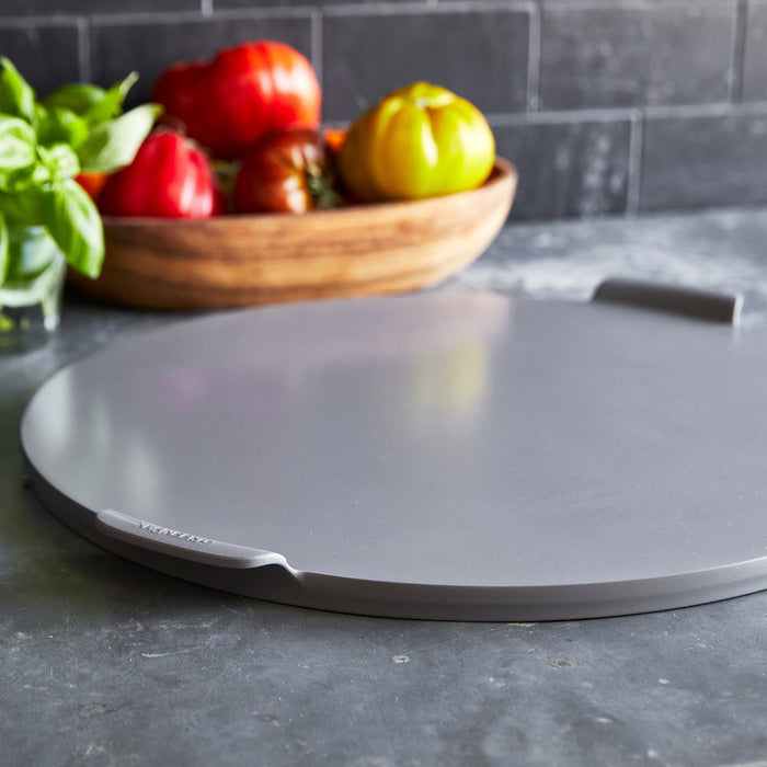 Gray 16.5-inch round pizza baker on a kitchen counter with fresh tomatoes and basil nearby.