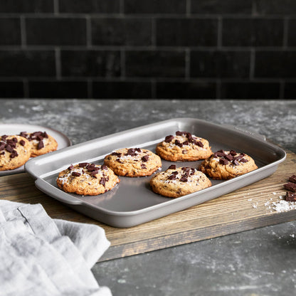Ceramic nonstick quarter sheet pan with six cookies on a gray counter, next to a plate and napkin.