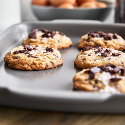 Four chocolate chip cookies on a ceramic nonstick quarter sheet pan set, topped with sea salt.