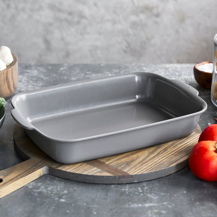 Gray 2-piece ceramic nonstick cake pan set on a wooden cutting board with assorted vegetables nearby.