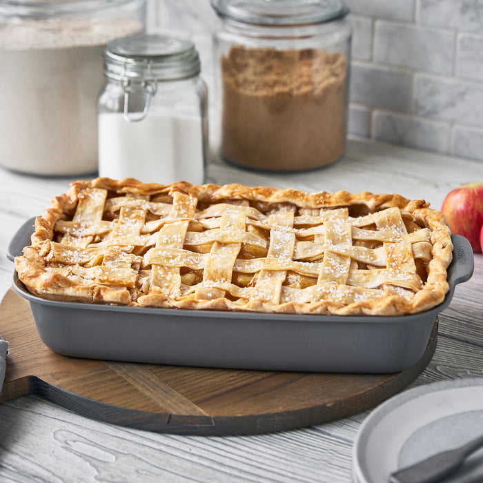 Ceramic nonstick cake pan set holding a lattice-topped pie, on a board with jars blurred in the background.