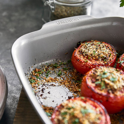 Stuffed tomatoes with herbs and breadcrumbs in a rectangular ceramic cake pan with light-colored interior.