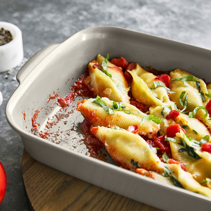 Ceramic nonstick cake pan with stuffed pasta shells in tomato sauce, set on a wooden board.