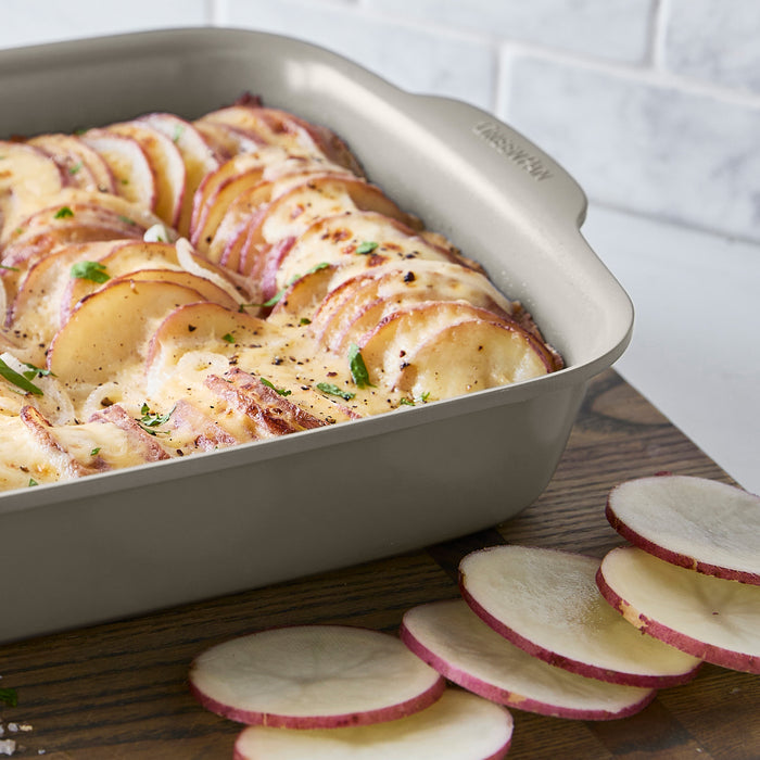 Taupe ceramic nonstick cake pan set, 2 pieces, shown with cheesy baked potato slices and assorted foods on board.