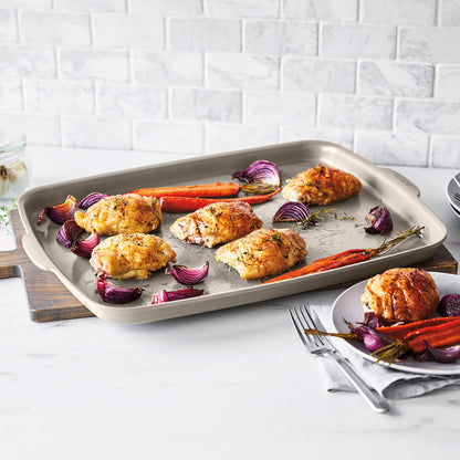 Roasted chicken thighs, carrots, and onions on a ceramic nonstick sheet pan set with pieces of the set shown nearby.