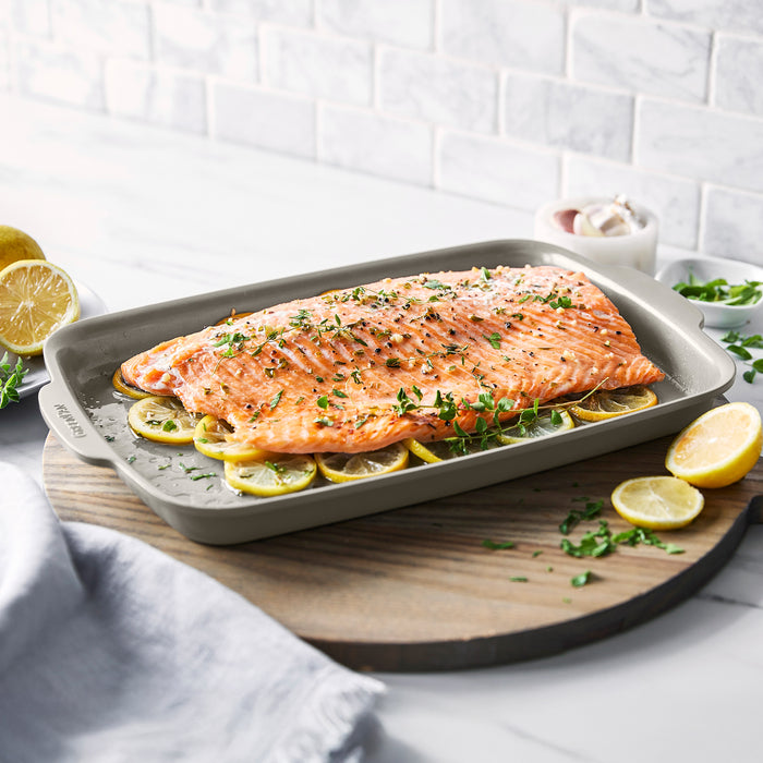 Baked salmon with herbs and lemon on a taupe ceramic nonstick 13x9 inch sheet pan.