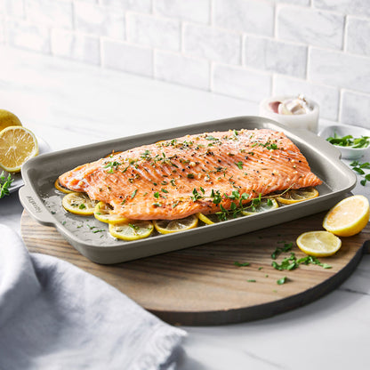 Baked salmon with herbs and lemon on a taupe ceramic nonstick 13x9 inch sheet pan.