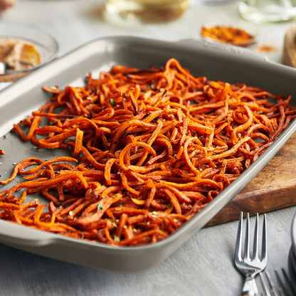 Sweet potato noodles in a white ceramic nonstick 13x9 quarter sheet pan on a table with two metal forks.