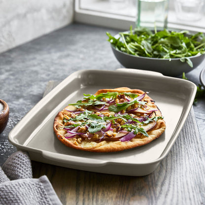 Ceramic taupe 6-piece bakeware set with flatbread pizza topped with arugula, red onions, and walnuts.