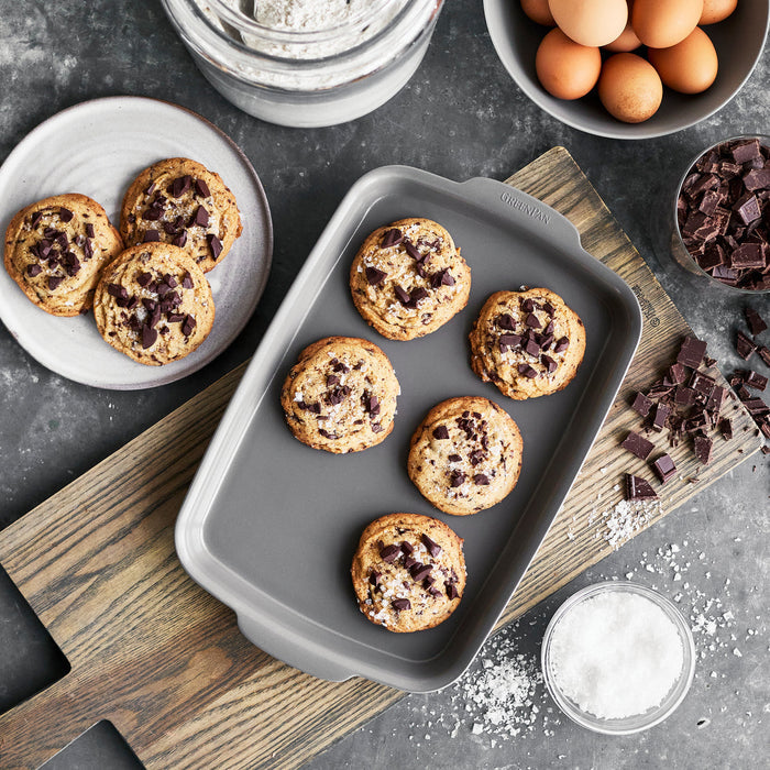 Gray ceramic nonstick 5-piece bakeware set with chocolate chip cookies, eggs, flour, and chocolate chunks.