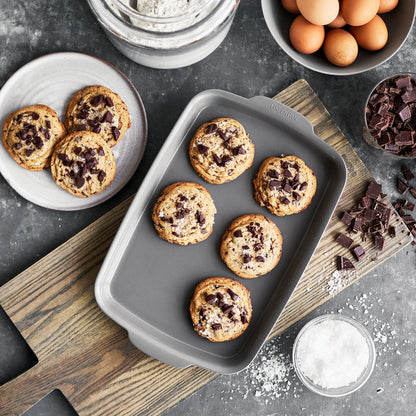 Gray ceramic nonstick 5-piece bakeware set with chocolate chip cookies, eggs, flour, and chocolate chunks.