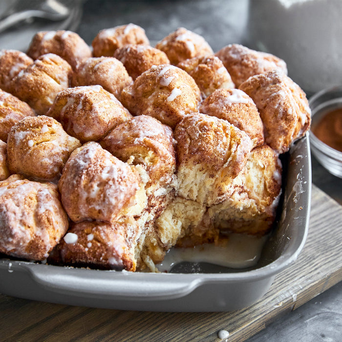 Cinnamon monkey bread with icing in a gray ceramic nonstick bakeware set, one piece missing from the set.