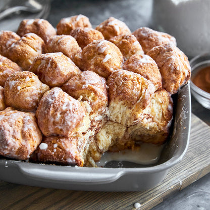 Cinnamon monkey bread with icing in a gray ceramic nonstick bakeware set, one piece missing from the set.