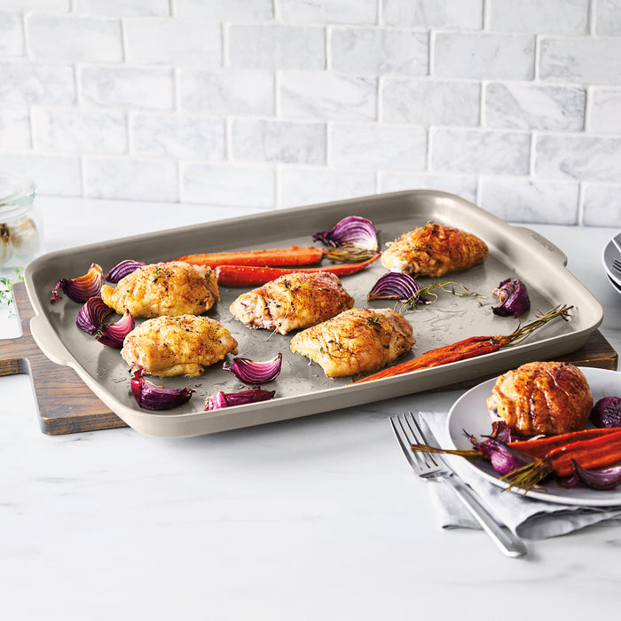 Ceramic nonstick 6-piece bakeware set in taupe with roasted chicken, carrots, onions, and a plate nearby.