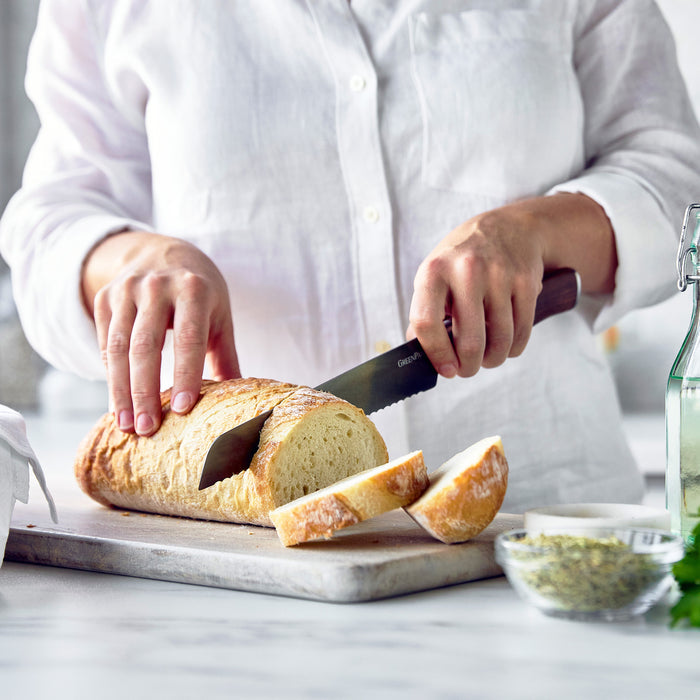 Person in a white shirt slicing bread with a knife featuring a walnut wood handle.