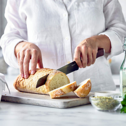 Person in a white shirt slicing bread with a knife featuring a walnut wood handle.