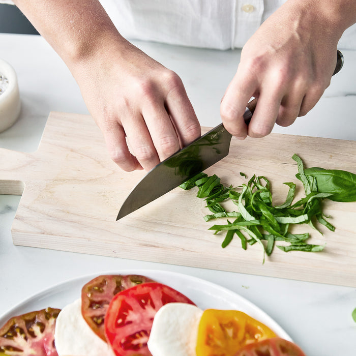 Basil being sliced with a Premiere Titanium Cutlery knife featuring a walnut wood handle on a wooden cutting board.