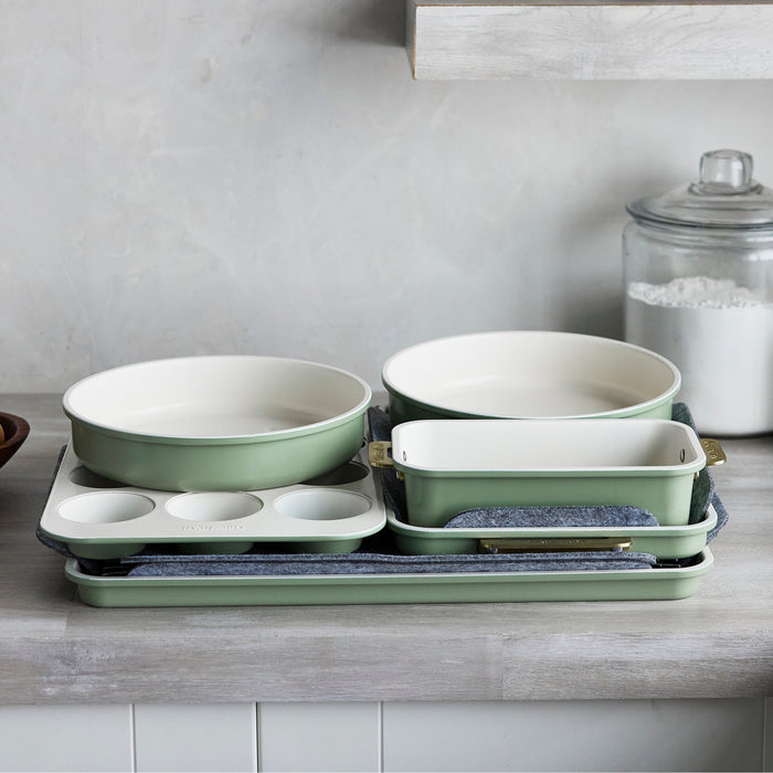 Sage green bakeware set of 8 pieces stacked on a kitchen counter next to a glass jar of flour.