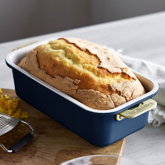 Loaf of bread in a blue loaf pan on a wooden surface with a white napkin and yellow flowers.