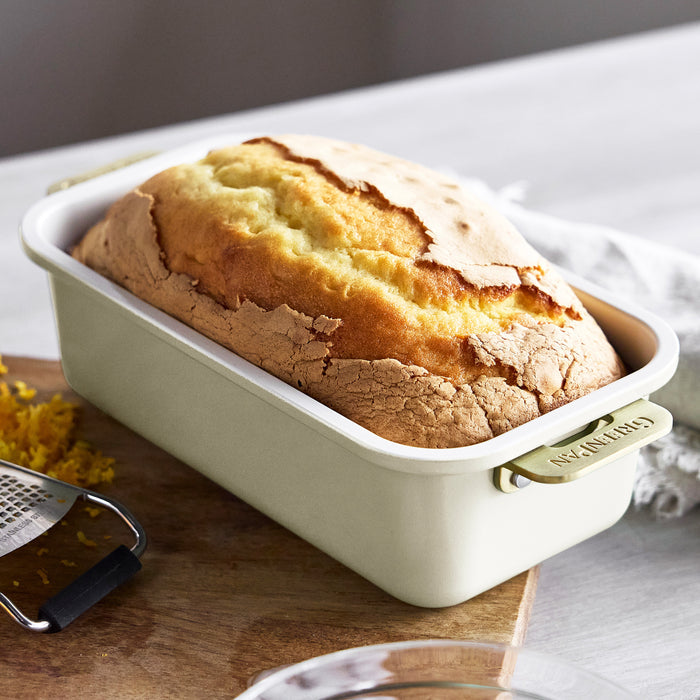 Loaf of cake in a cream loaf pan on a wooden cutting board with a grater.