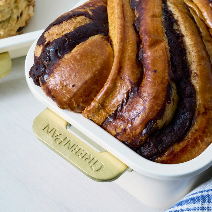 Braided bread with chocolate swirls in a cream loaf pan on a light surface.