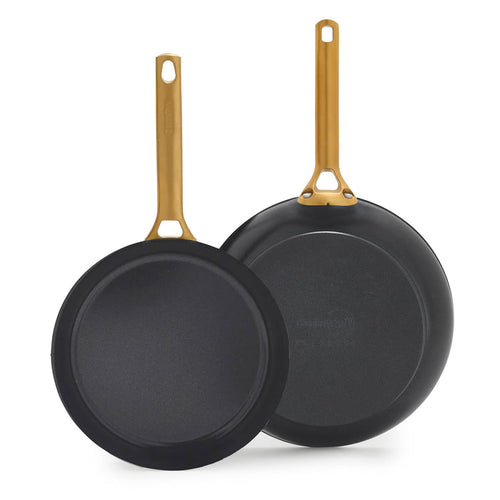Two black frying pans with gold handles on a white background