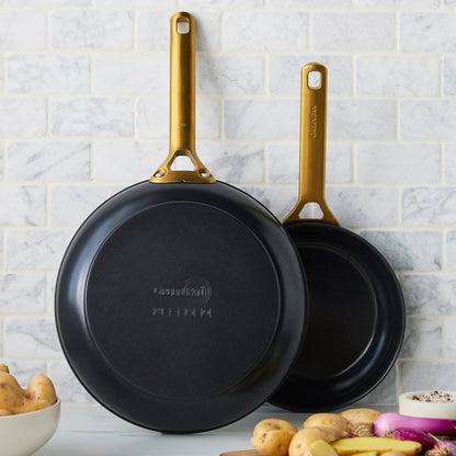 Two black frying pans with gold handles on a kitchen counter.