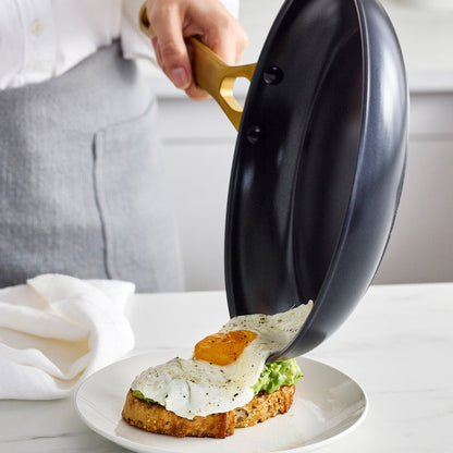 Person pouring an egg from a black frying pan onto toast on a white plate.