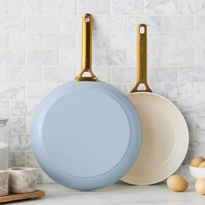 Two light blue frying pans with gold handles on a kitchen counter.