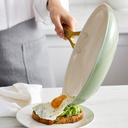 Person using a green frying pan to place an egg on a piece of toast.