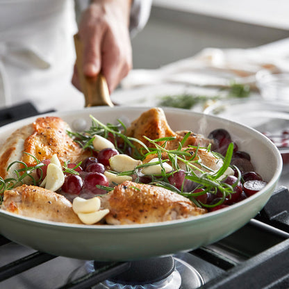 Chicken dish with grapes and herbs in a green frypan on a stove