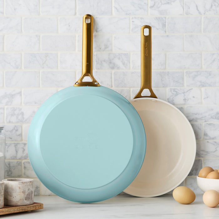 Two light blue frying pans on a kitchen counter with a marble backsplash.