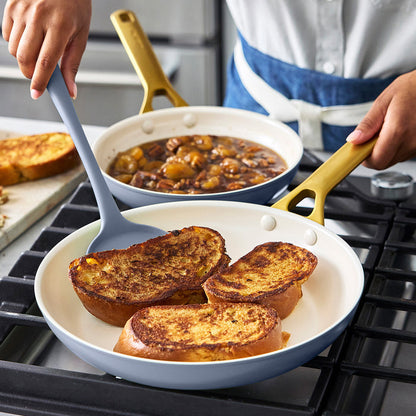 Person cooking French toast in a blue frying pan on a stove with a blue spatula.