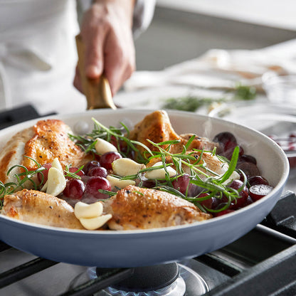 Roasted chicken with grapes and herbs in a blue frypan on a stove