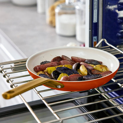 Dark orange frying pan with sausages and potatoes in an oven