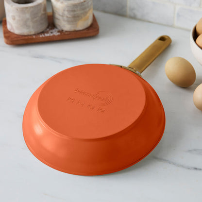 Dark orange frying pan with a gold handle on a marble countertop