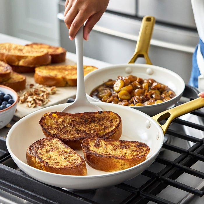 Taupe gray frying pan with a gold handle containing slices of toasted bread on a stovetop.