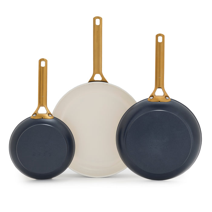 Three dark blue frying pans with gold handles on a white background