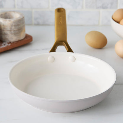 Taupe gray frying pan with a gold handle on a kitchen counter with eggs in the background.