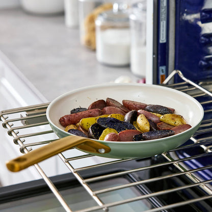 Sage green frying pan with sausages and vegetables in an oven