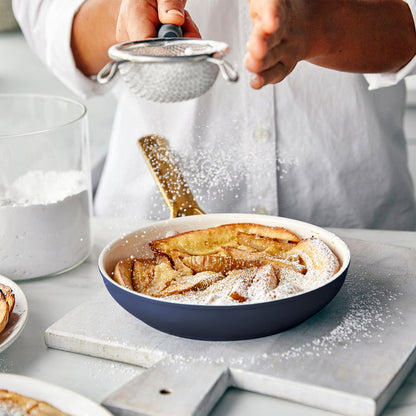 Person dusting a dish of apple slices with powdered sugar using a sifter.
