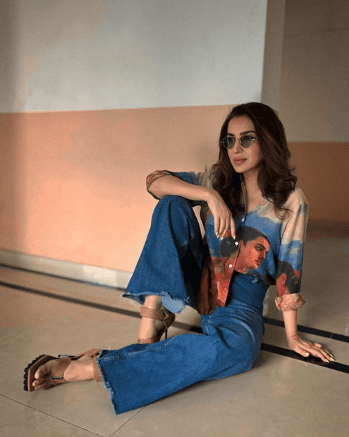 Woman wearing the Shakuntala shirt with blue jeans, sitting on the floor against a wall, front view