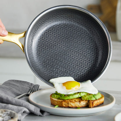 Gold ceramic nonstick frypan held over a plate with avocado toast and a sunny-side-up egg.