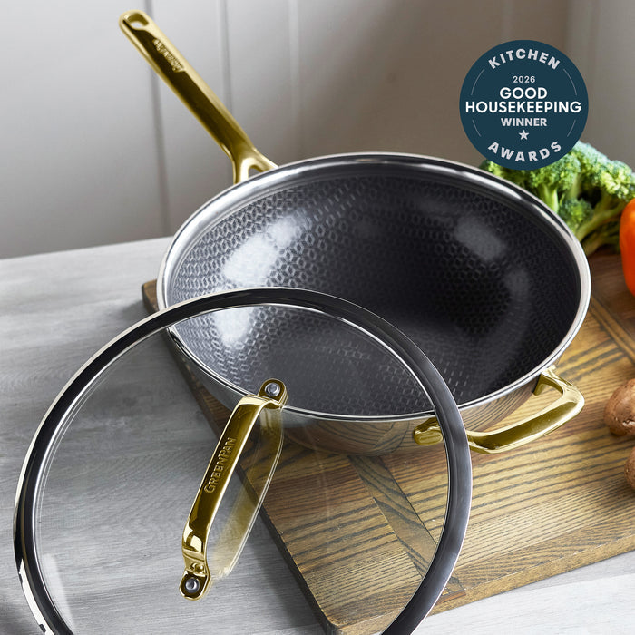 Gold ceramic 12-inch wok with matching gold handle and clear glass lid, displayed on a table.