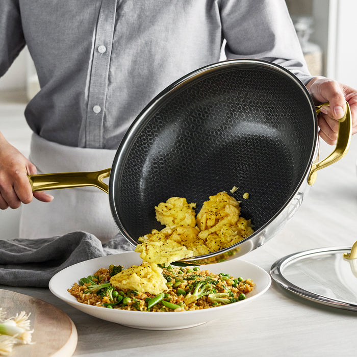 Scrambled eggs being poured from a Spectra Gold ceramic nonstick wok with lid onto a bowl of fried rice.