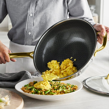 Scrambled eggs being poured from a Spectra Gold ceramic nonstick wok with lid onto a bowl of fried rice.